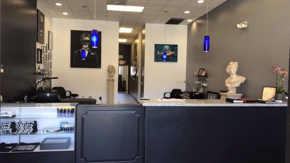 The front counter at Palace Art Tattoo: a merch case, framed art, a marble bust and blue pendant lamps
