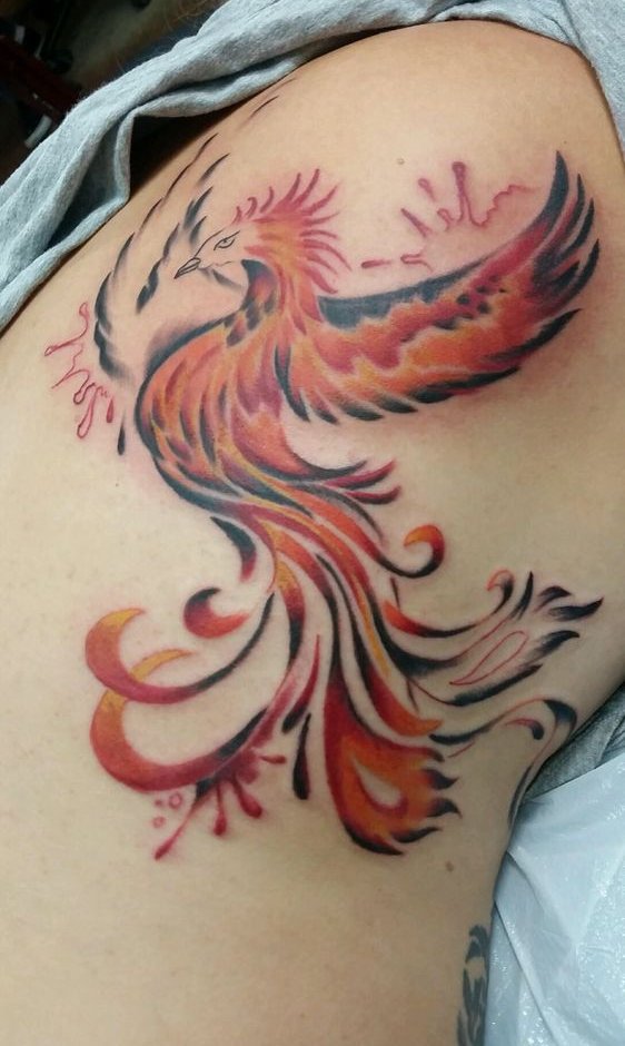 A red and orange phoenix in flight across a shoulder blade, with ink splashes