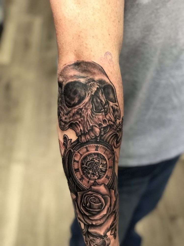 A black-and-grey skull above an open pocket watch and a rose on a forearm